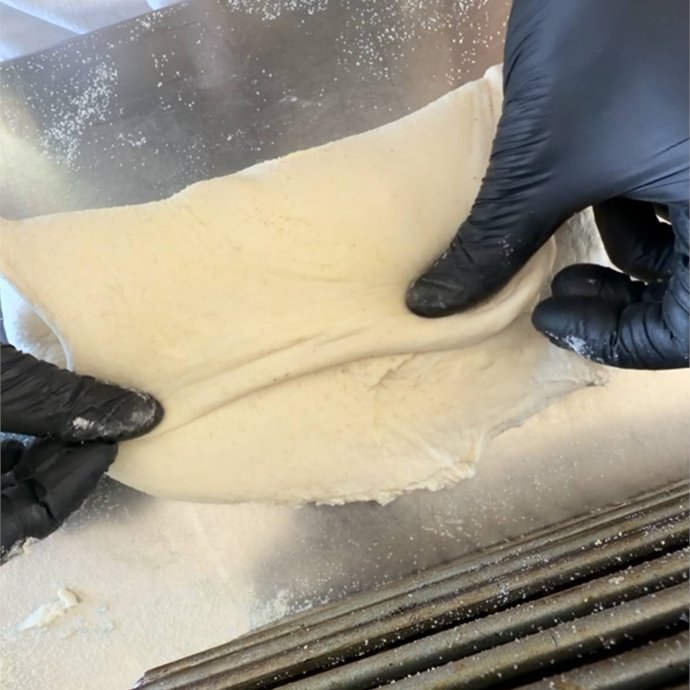 Mani che stirano il lembo inferiore dell'impasto prima di piegarlo verso il centro